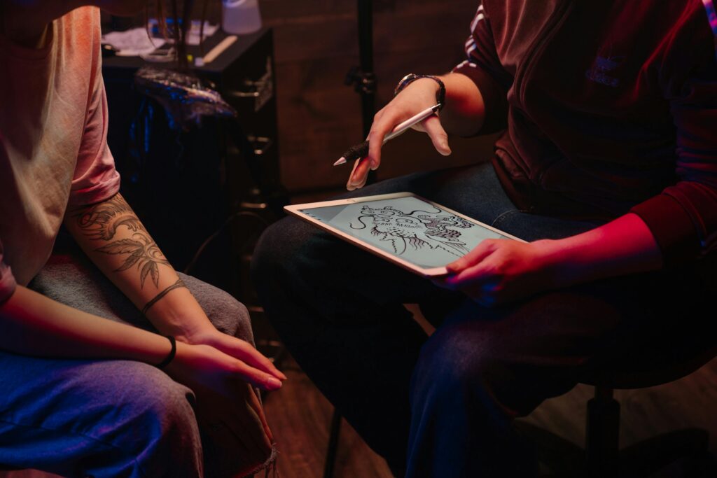Tattoo artist consulting with client, sketching dragon design in studio.